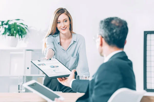 Young attractive businesswoman passing clipboard with documents to partner — Stock Photo