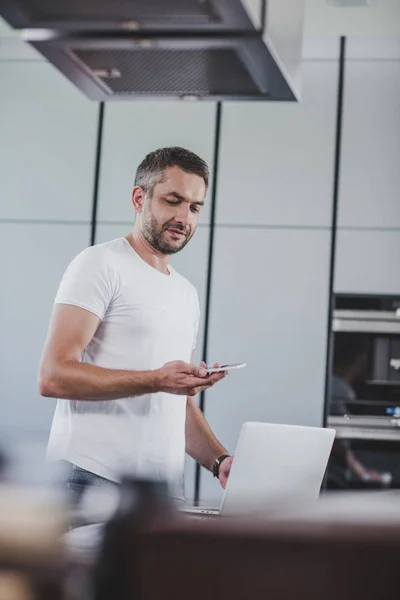 Bel homme regardant smartphone dans la cuisine — Photo de stock