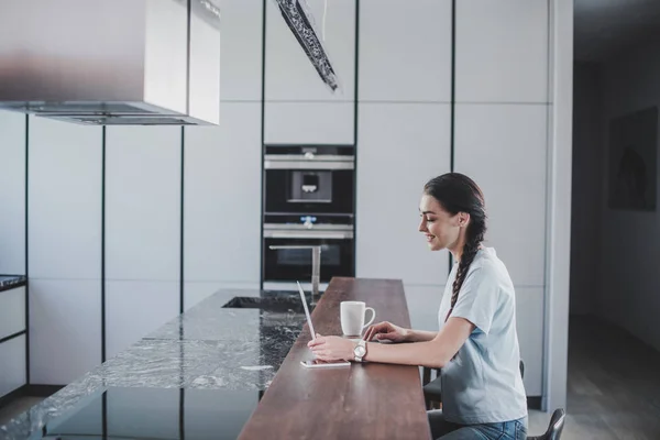 Side view of beautiful smiling woman using laptop in kitchen — Stock Photo