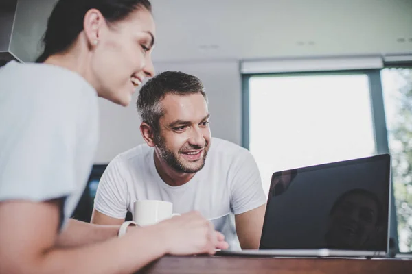 Sorrindo casal olhando para laptop com tela em branco na cozinha — Fotografia de Stock