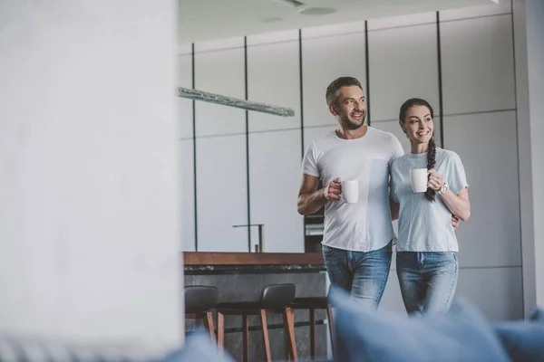 Селективное внимание улыбающейся пары с чашками кофе на кухне дома — стоковое фото
