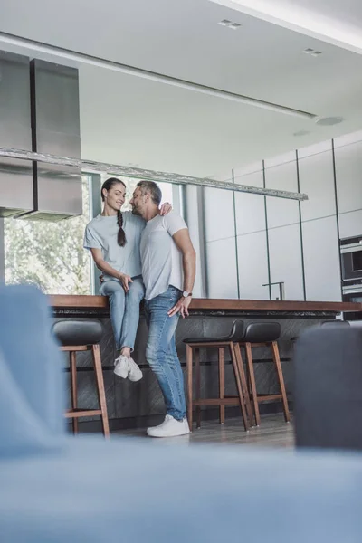 Vista de ángulo bajo de la atractiva mujer sentada en el mostrador de la cocina y abrazando novio en casa - foto de stock