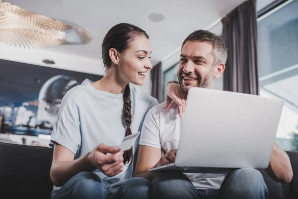 Счастливая пара с ноутбуком делать покупки через кредитную карту дома — стоковое фото