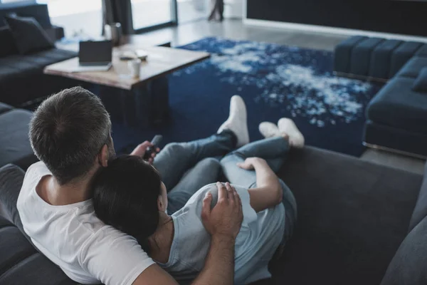 Foco seletivo do homem adulto com controlador remoto abraçando namorada e assistindo tv no sofá em casa — Fotografia de Stock
