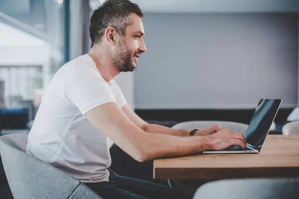 Vista lateral de belo freelancer masculino usando laptop com tela em branco em casa — Fotografia de Stock