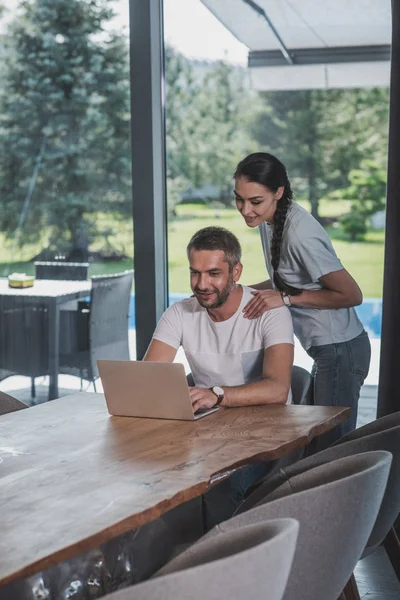 Attraktive Frau umarmt Freund, während er zu Hause Laptop benutzt — Stockfoto