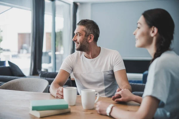 Paar hält Händchen und schaut zu Hause bei Kaffee und Büchern vom Tisch weg — Stockfoto