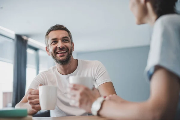 Bajo ángulo vista sonriente pareja bebiendo café y hablando en la mesa en casa - foto de stock