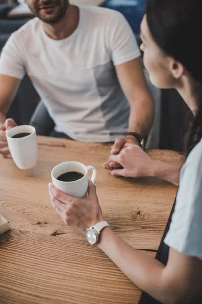 Visão parcial do casal beber café e de mãos dadas à mesa — Fotografia de Stock