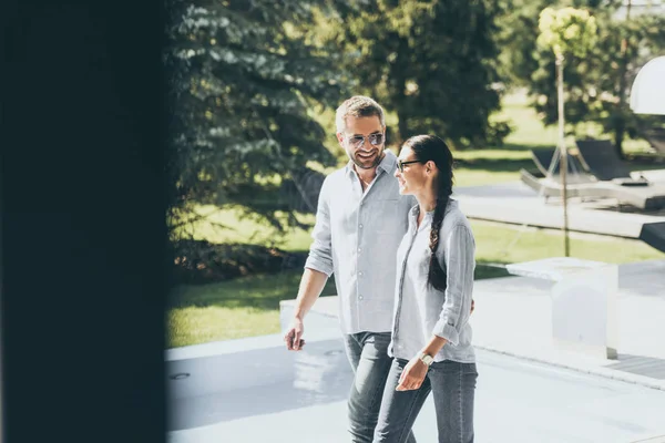 Улыбающаяся пара в солнечных очках, идущая в загородный дом — стоковое фото
