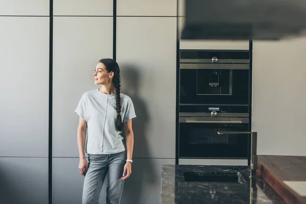Attraente giovane donna guardando lontano in cucina a casa — Foto stock