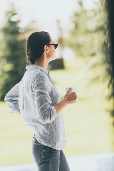 Side view of woman in sunglasses standing with cup of coffee outdoors — Stock Photo