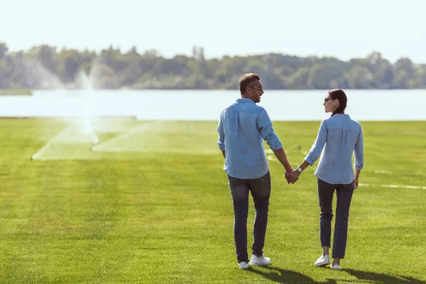 Пара в солнечных очках держатся за руки и смотрят друг на друга на лужайке под открытым небом — стоковое фото