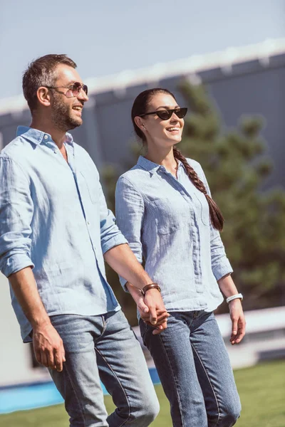 Casal feliz em óculos de sol de mãos dadas e andando ao ar livre — Fotografia de Stock