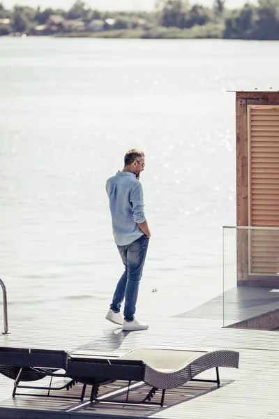 Hombre adulto hablando en teléfono inteligente cerca del lago en la casa de campo - foto de stock