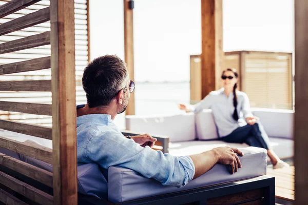 Adult man in sunglasses sitting on sofa and talking to girlfriend at country house — Stock Photo