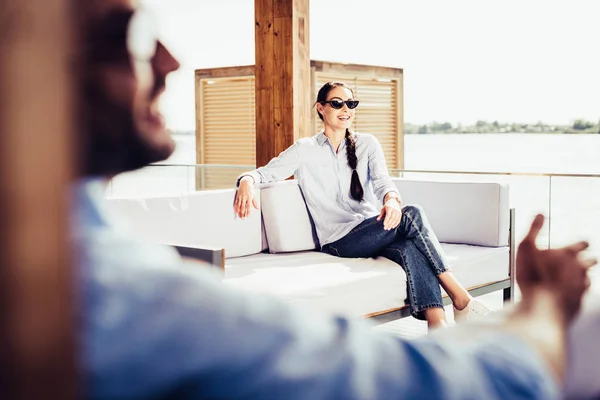 Foco seletivo de mulher sorridente em óculos de sol no sofá, enquanto seu namorado sentado perto da casa de campo — Fotografia de Stock