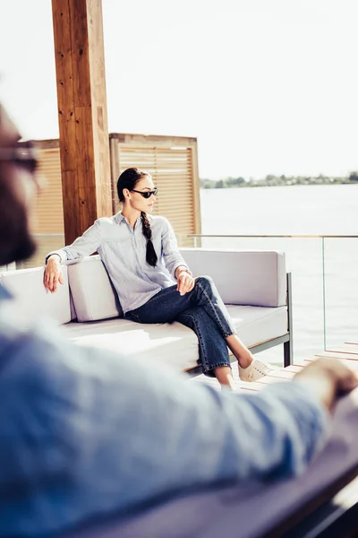 Attraktive Frau mit Sonnenbrille auf der Couch, während ihr Freund in der Nähe im Landhaus sitzt — Stockfoto