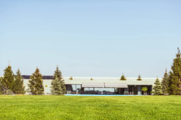 Foco seletivo de gramado verde e casa de campo moderna sob céu azul claro — Fotografia de Stock