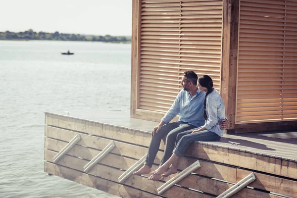 Couple embracing each other and sitting on wooden pier near lake — Stock Photo