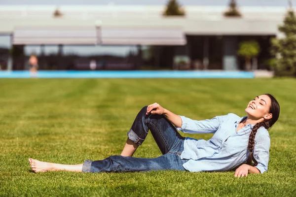 Selective focus of happy young woman resting on grass in front of country house — Stock Photo