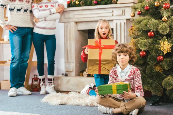 Plan recadré de parents se tenant derrière les enfants avec des cadeaux de Noël à la maison — Photo de stock