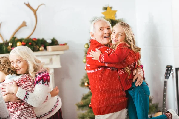 Avós felizes abraçando com crianças no Natal em casa — Fotografia de Stock