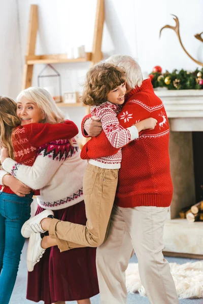Lächelnde Großeltern, die sich an Weihnachten zu Hause mit ihren Kindern umarmen — Stockfoto