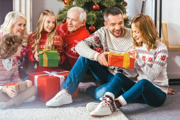 Beautiful family with gift boxes sitting on floor of living room during christmas — Stock Photo