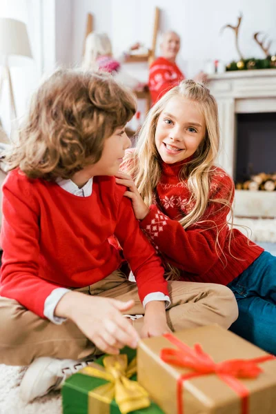 Adorables hermanos en suéteres rojos sentados en el suelo con cajas de Navidad - foto de stock