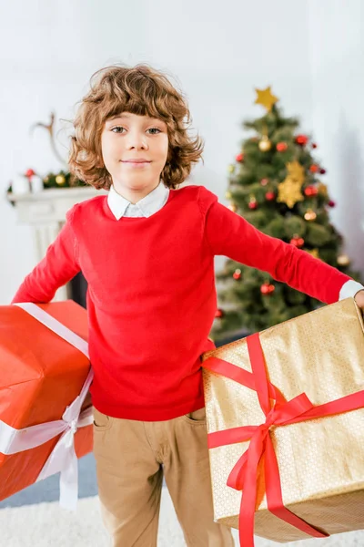 Lindo niño feliz sosteniendo grandes cajas de Navidad y mirando a la cámara - foto de stock