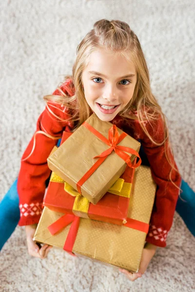 High angle view of beautiful happy child sitting on floor with stack of christmas gift boxes — Stock Photo