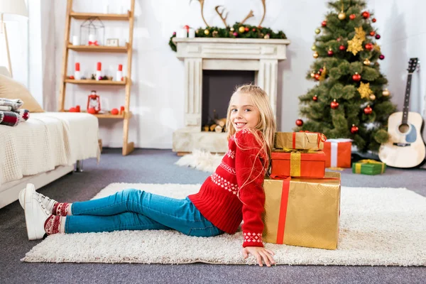 Beautiful happy child leaning on stack of christmas gift boxes while sitting on floor — Stock Photo