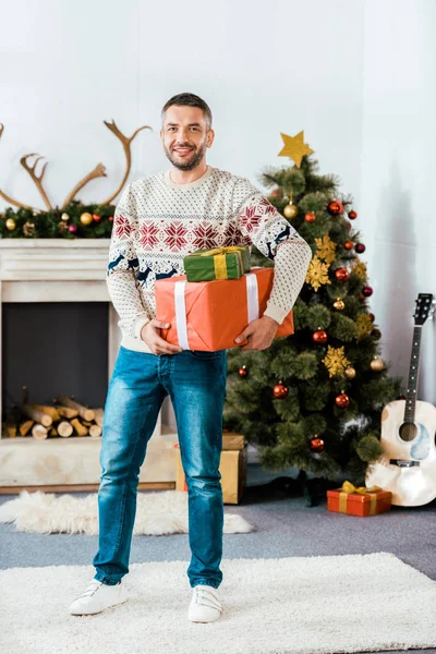 Красивый бородатый мужчина в рождественском свитере с подарочными коробками, смотрящий в камеру — стоковое фото