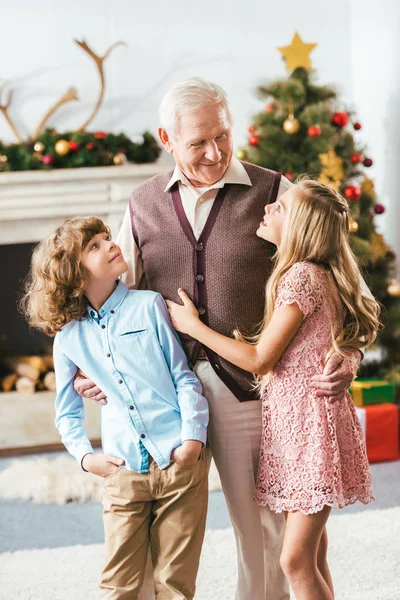 Abuelo feliz abrazar a los niños en la sala de estar decorada de Navidad en casa - foto de stock