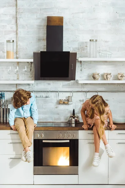 Frères et sœurs assis sur la table de cuisine et regardant four de cuisson — Photo de stock