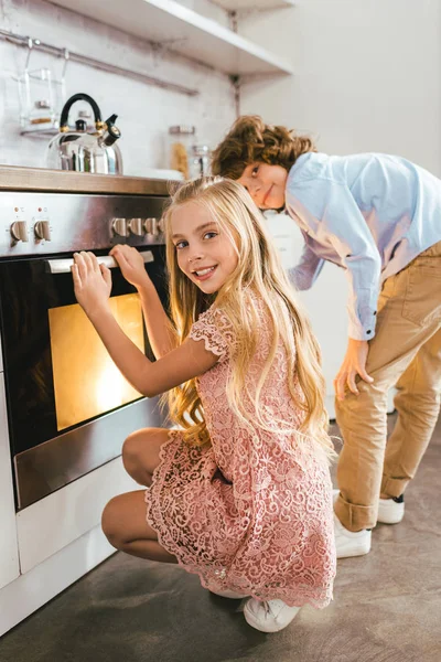 Счастливые обожаемые братья и сестры, стоящие возле духовки на кухне — стоковое фото
