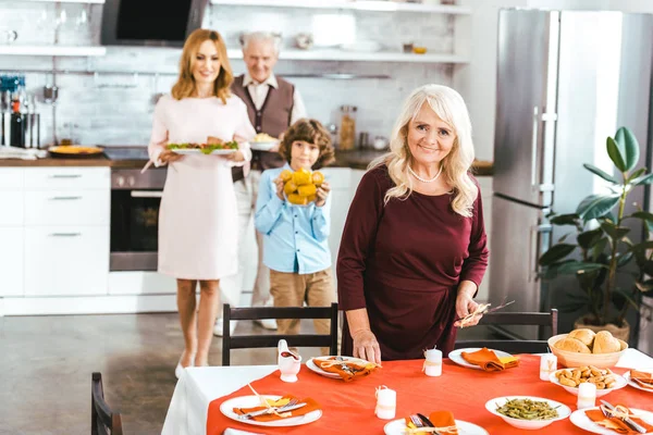Grandparents with adult daughter and little grandson serving table for thanksgiving dinner — Stock Photo