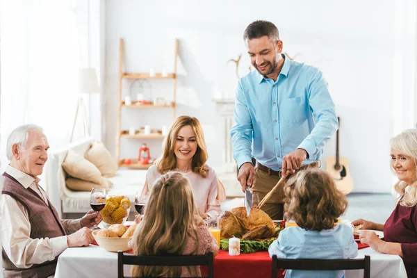 Gran familia teniendo deliciosa cena de acción de gracias juntos en casa mientras padre corte pavo - foto de stock