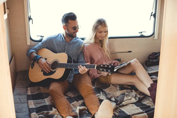 Happy boyfriend playing on guitar while girlfriend holding vinyl record inside campervan — Stock Photo