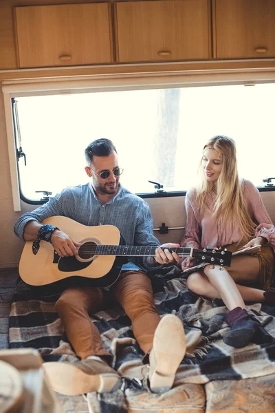 Handsome man playing on guitar while girlfriend holding vinyl record inside trailer — Stock Photo