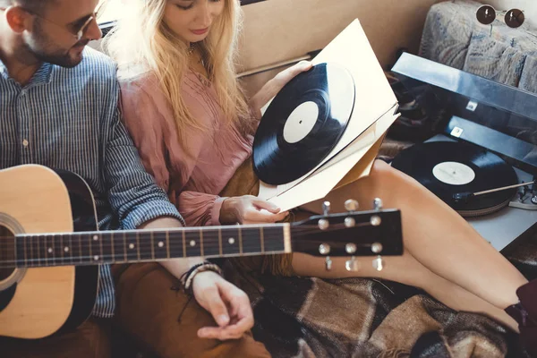 Hippie couple with acoustic guitar and vinyl records sitting inside trailer — Stock Photo