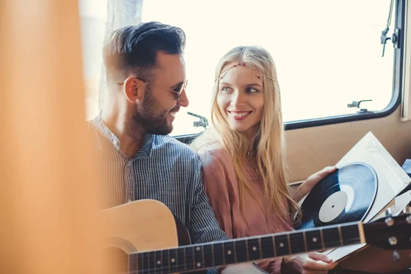 Beautiful hippie couple resting inside trailer with acoustic guitar and  vinyl record — Stock Photo