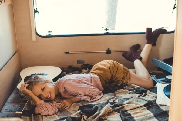 Attractive laughing girl lying inside trailer with acoustic guitar and vinyl player — Stock Photo
