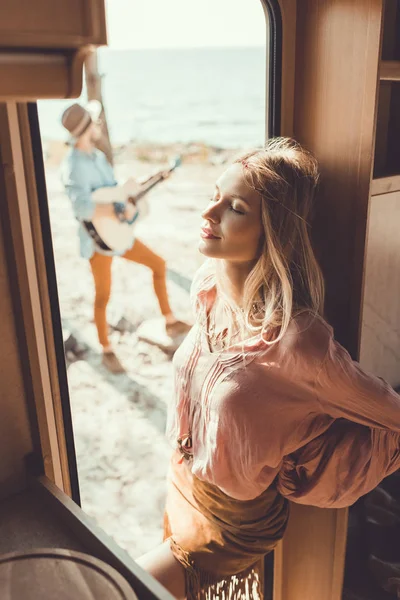 Selective focus of girl standing in door of trailer and listening man playing guitar — Stock Photo