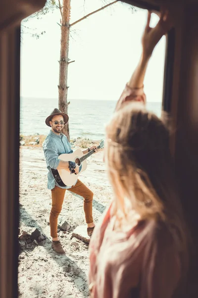 Selective focus of girl standing in door of campervan while man playing guitar — Stock Photo
