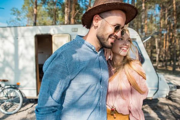 Hippie couple embracing near trailer in forest — Stock Photo