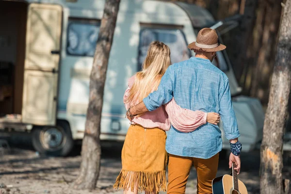 Vista trasera de pareja hippie abrazando y sosteniendo la guitarra cerca de autocaravana - foto de stock