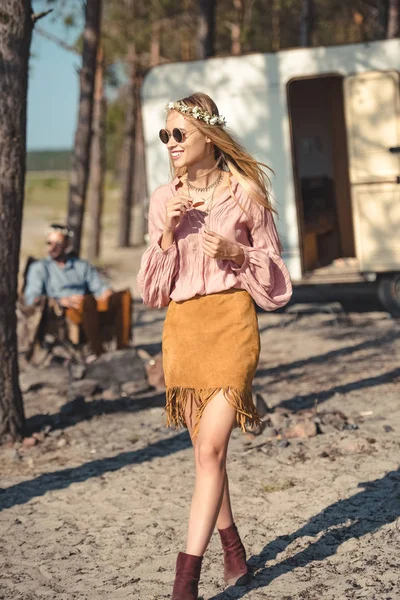 Hippie chica en corona, hombre sentado cerca remolque en bosque detrás - foto de stock