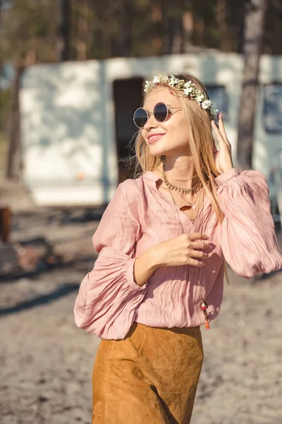 Hermosa chica hippie sonriente en corona y gafas de sol posando cerca campervan - foto de stock